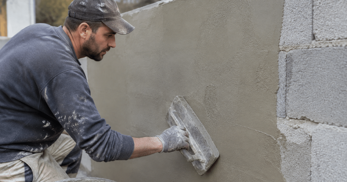 Maçon appliquant enduit lissé sur mur bloc béton vertical
