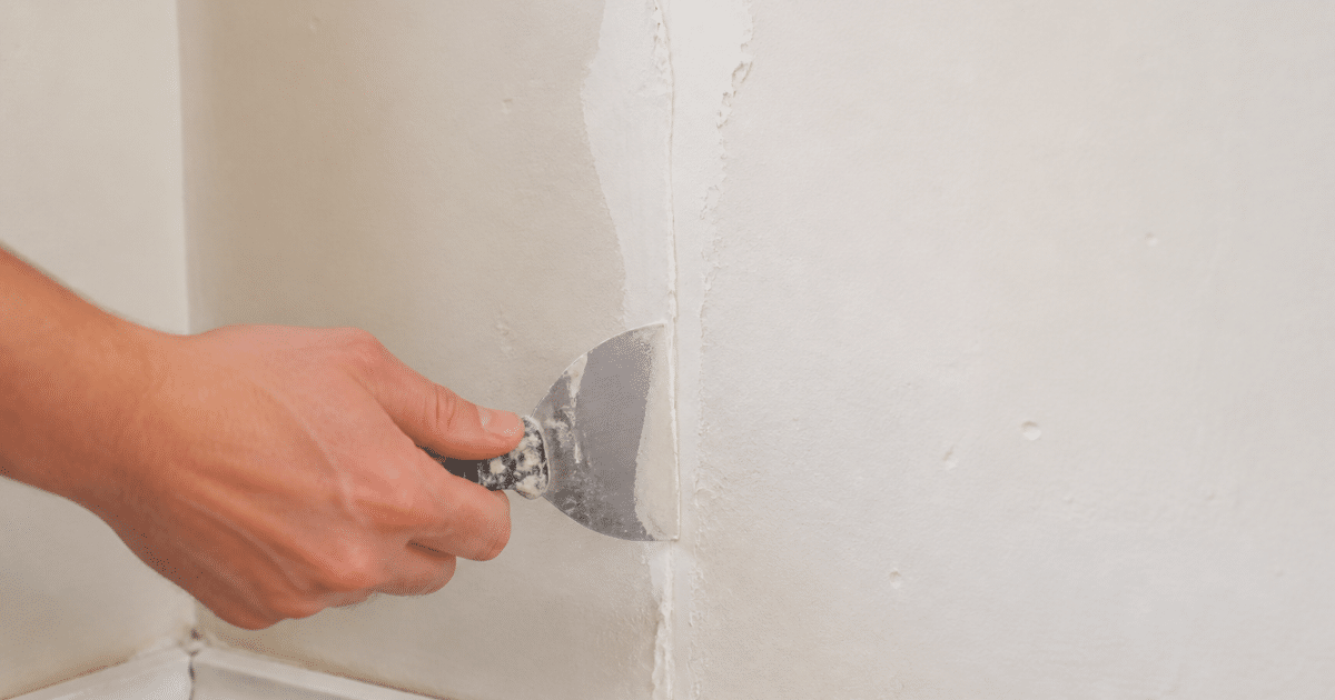 Main appliquant composé de rebouchage blanc sur fissure murale verticale
